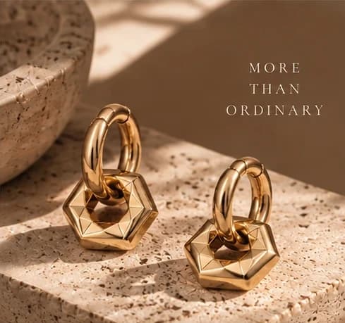 Two chunky gold hoops with faceted hexagonal charms on a travertine block