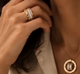A stacked gold ring, a circle pendant and a chain bracelet worn with a cream shirt