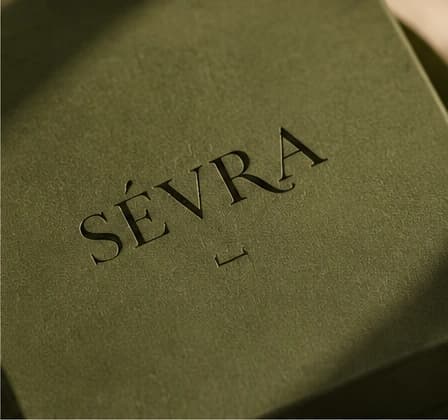 The SÉVRA wordmark blind-debossed into the lid of a dark green gift box